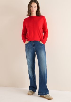 Röd långärmad topp med rund halsringning, ihop med ljus tvättade utsvängda jeans och beige skor, med sidofickor och en avslappnad passform.