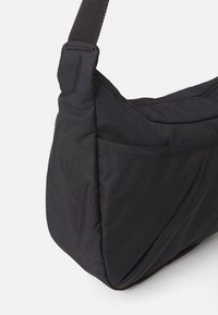 Black nylon shoulder bag with an adjustable strap, zippered top, and slip pocket on the side against a white background.