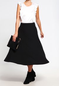 Top in satin bianco con maniche a volant, abbinato a una gonna nera a trapezio. L'outfit è completato da stivaletti neri alla caviglia e una piccola borsa a tracolla.