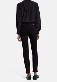 Jeans negros de corte ajustado, elaborados en denim. La parte trasera cuenta con dos bolsillos y una sutil etiqueta de la marca. Combinados con una camisa negra de manga larga.