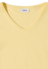 T-shirt jaune clair à col en V avec des coutures visibles et une étiquette blanche indiquant "CECIL" au niveau de l'encolure.