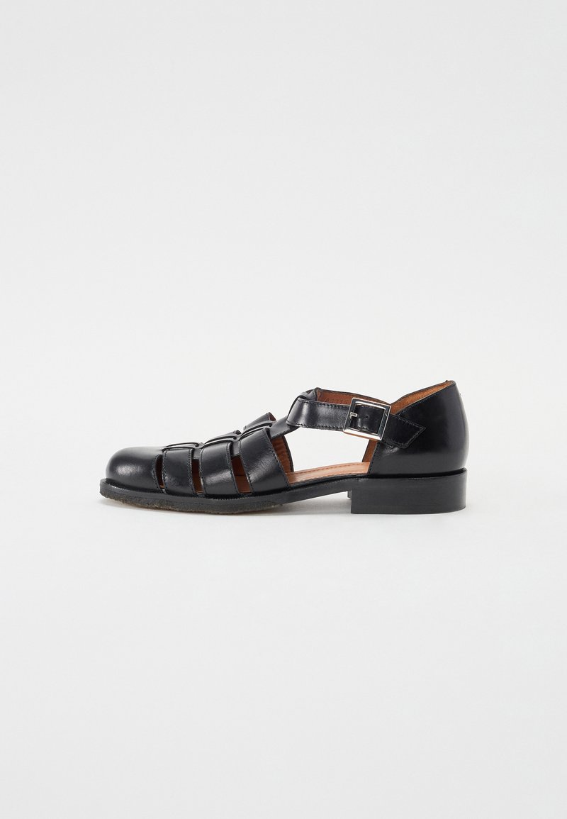 Black leather sandal with crisscross straps, open sides, and a small heel. Features a buckle closure and a smooth, shiny texture.