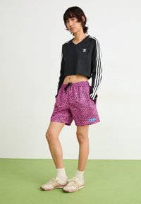 Top nero a maniche lunghe e cropped con strisce bianche, abbinato a pantaloni corti a stampa leopardata rosa con un accento blu. Sneakers beige e calzini bianchi.