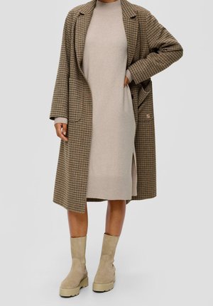 Cappotto lungo a quadri marroni sopra un vestito a coste beige, abbinato a stivaletti alla caviglia con suola chunky beige chiaro.