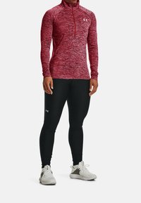 Maglia sportiva a maniche lunghe rosso mélange con collo a mezza cerniera, abbinata a leggings neri. Accenti di logo bianco su entrambi i capi. Scarpe da ginnastica.