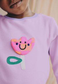 Lilla pikkade varrukatega särk mitmevärvilise, naeratava õiepistmega, millel on roosad kroonlehed, valge varreosa ja roheline leht.