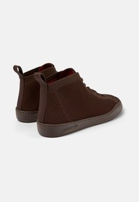 Hnědé vysoké tenisky vyrobené z texturované síťoviny, s gumovou podrážkou a poutky na zadní straně. Šněrovací design, minimalistický styl.