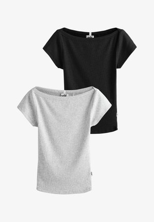 Junge Frau mit lockigem Haar trägt ein hellgraues, eng anliegendes Croptop, blaue Shorts und ein blau gestreiftes Hemd, das um die Taille gebunden ist.
