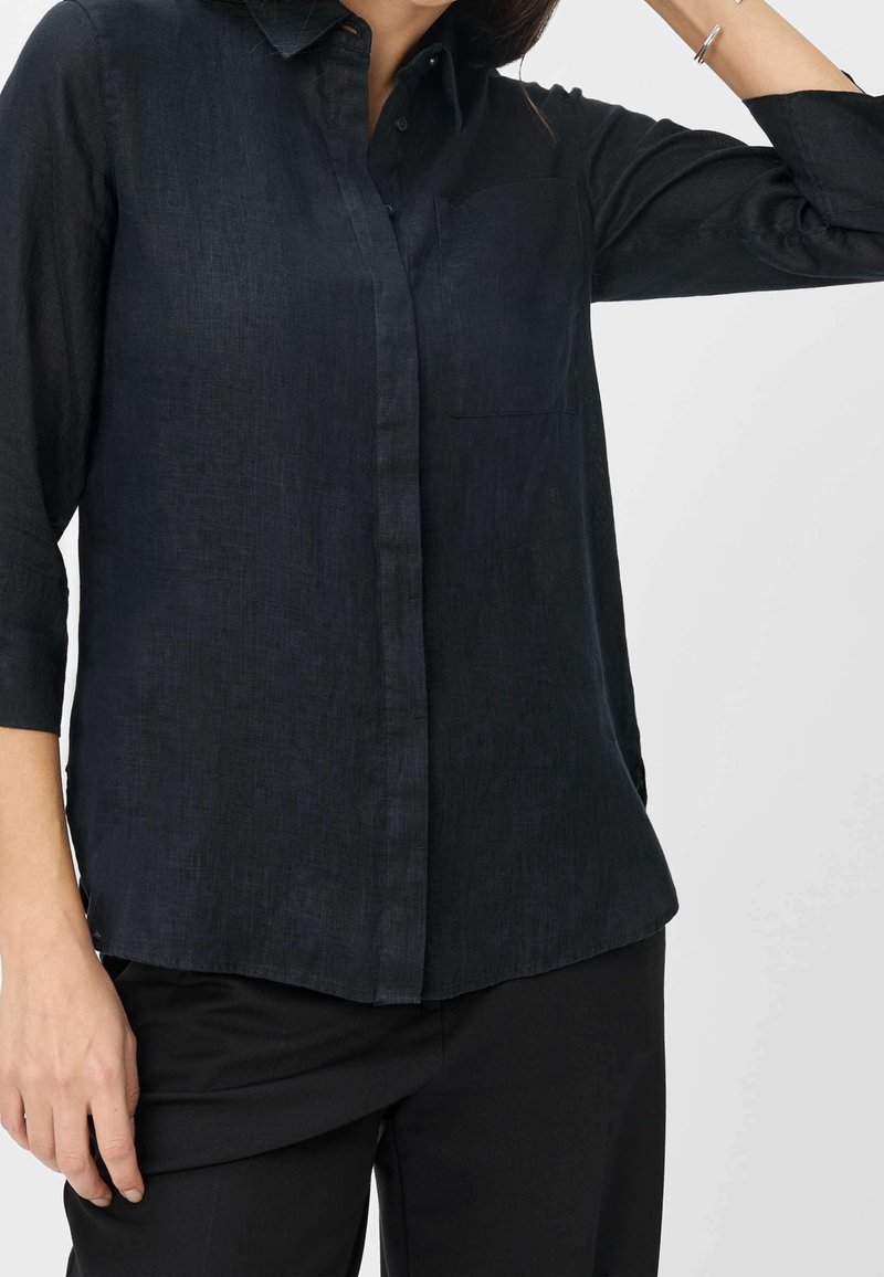 Chemise noire à boutons avec col, manches longues et poche poitrine. Fabriquée dans un tissu léger et texturé. Finition lisse.