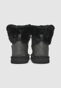 Une paire de bottines noires pailletées avec une épaisse bordure en fourrure noire autour du haut, vues de l'arrière.