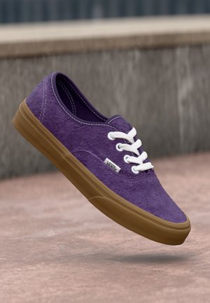 Purple canvas sneakers with a textured finish, white laces, and brown rubber soles. Features a small brand logo tag on the side.
