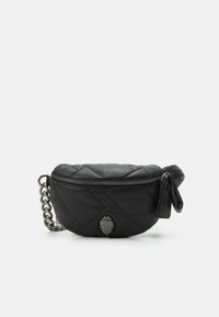 Černá prošívaná kabelka s kulatým tvarem, stříbrným řetízkovým popruhem a dekorativním kovovým emblémem. Má zapínání na zip a boční střapec.