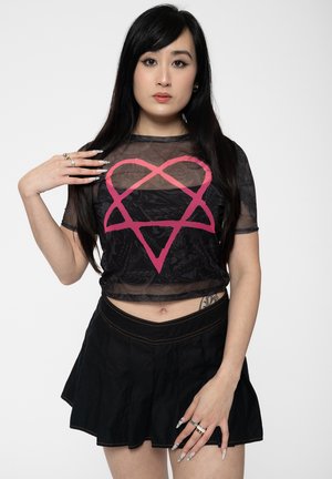 Black mesh crop top with a pink heart design, paired with a black pleated skirt. Notable details include short sleeves and a fitted silhouette.