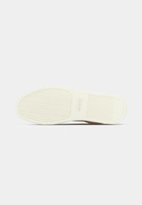 Semelle de chaussure avec une base en caoutchouc blanc texturé, ornée d'un motif en chevrons et du logo "GUESS" en relief sur le côté.