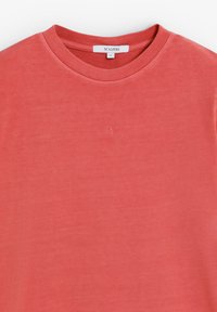 Camiseta corta de manga corta color coral, hecha de algodón suave. Presenta un cuello redondo y un pequeño logo bordado en el pecho. Talla S.