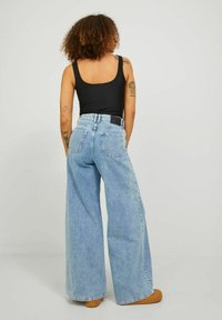 Világoskék, széles lábú farmernadrág magas derékkal és hátsó zsebekkel, denim anyagból készült. Látható fekete trikó, kerek nyakkivágással.