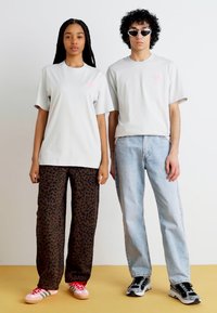 Ljust grå T-shirts med rosa logga, kombinerat med leopardmönstrade byxor och denimjeans. Randiga sneakers och solglasögon fulländar outfiten.