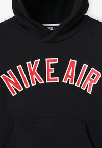 Černá mikina s kapucí s nápisem „NIKE AIR“ výrazným červeným písmem s bílým obrysem. Hladká látka a přední kapsa ve tvaru klokánka.