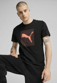 T-shirt in cotone nero con un motivo a griglia rossa e logo Puma. Il tessuto appare liscio, con maniche corte e un design a colletto girocollo.