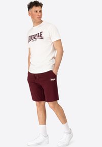 Hvid bomulds-T-shirt med maroon "Lonsdale London" logo, parret med maroon shorts med sidelommer og matchende logo. Hvide sneakers.