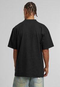 Black oversized t-shirt with short sleeves, crew neck, and smooth fabric texture. Notable detail includes a small logo accent near the hem.