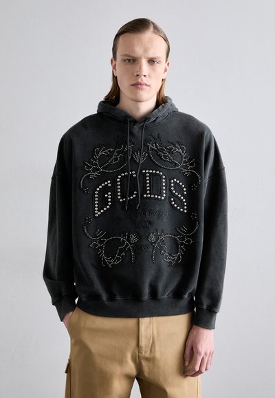 Black hoodie with rhinestone embellishments and a graphic design. Features a drawstring hood and ribbed cuffs. Paired with beige pants.