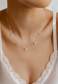 Collier en argent avec cinq petits pendentifs en forme de papillon, ornés de pierres transparentes. Chaîne délicate au design simple, porté sur un décolleté en dentelle.