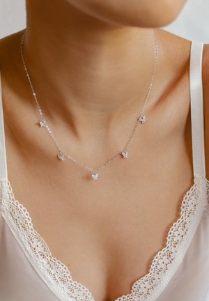 Collar de plata con cinco pequeños colgantes de mariposas, con piedras transparentes. Cadena delicada con un diseño sencillo, llevado sobre un escote de encaje.