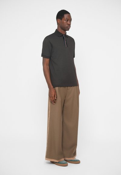 Σκούρο πόλο μπλουζάκι με γιακά, διαθέτοντας πολύχρωμη ρίγα στον λαιμό. Συνδυασμένο με φαρδιά καφέ παντελόνια και teal �παπούτσια.