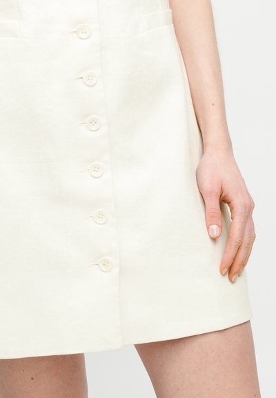 Λευκό λινό φόρεμα με ευθεία γραμμή, διαθέτοντας έξι κουμπιά στο μπροστινό μέρος, δύο πλαϊνές τσέπες και λείο, υφασμάτινο τελείωμα.