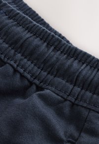 Artimas tamsiai mėlynos medžiagos vaizdas su elastingu juosmens diržu ir matomomis siuvimo detalėmis ant šviesios fono.