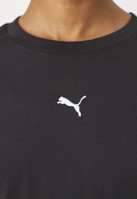 T-shirt noir à col rond avec un petit logo blanc de chat sautant centré sur la poitrine.