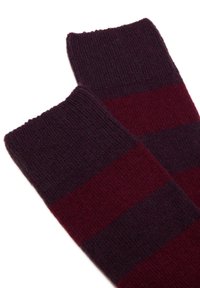 Un paio di calze lavorate a maglia con ampie righe orizzontali di colore viola scuro e bordeaux su uno sfondo bianco.