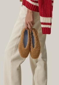 Scarpe slip-on marroni, morbide e tuftate, con una texture soffice e una forma arrotondata. Presentano un rivestimento interno blu visibile all'apertura e nessuna attrezzatura visibile.