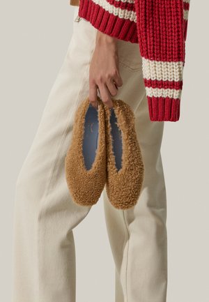 Chaussures plates en peluche de couleur marron, avec une texture douce et une forme arrondie. Elles ont une doublure intérieure bleue visible à l'ouverture et aucun matériel visible.