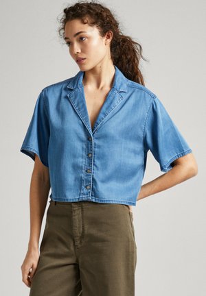 Camicetta di jeans cropped in azzurro chiaro, con maniche corte, colletto a punta e chiusura frontale a bottoni. Tessuto morbido e liscio.