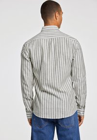 Grå og hvid stribet langærmet skjorte med knap-ned krave, blød tekstur og rundet kant, der er parret med blå denim jeans.