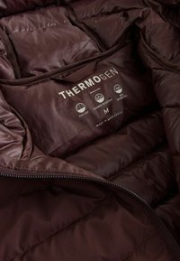 Barna steppelt dzseki sima textúrával, amelyen a "THERMOGEN" felirat, M-es méret és információk találhatók a zuhanyállóságról és a tolltöltetről.