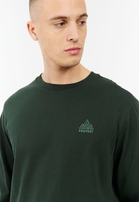 Donkergroen lange mouw t-shirt van katoen, met een klein berglogo in lichtgroen op de borst en een ronde halsontwerp.