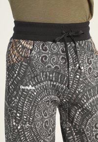 Czarne spodnie sportowe z wzorem w kształcie okręgów i różnymi fakturami. Dopasowany pasek w talii z sznurkiem. Logo na nodze.