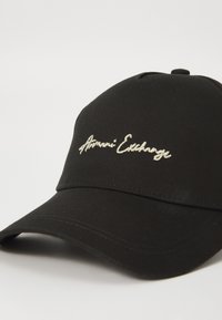 Sort kasket lavet af stof med en buet skygge. Har hvidt broderet tekst "Harmoni Exchange" foran. Klassisk design, justerbar bagside.