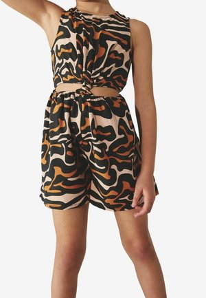 Enfant portant une combinaison sans manches à motif animalier avec un nœud à l'avant et une découpe à la taille, debout devant un fond uni.