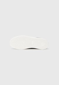 Sneaker-Sohle mit strukturiertem, weißem Gummiprofil, das kreisförmige, hexagonale und gekrümmte Rillenmuster auf weißem Hintergrund zeigt.