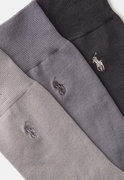 Τρία ζευγάρια κάλτσες σε σκούρο γκρι, μεσαίο γκρι και ανοιχτό γκρι. Κάθε κάλτσα διαθέτει υφασμένο μανίκι και ένα μικρό κεντημένο λογότυπο.
