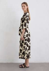 Floral dress in cream with large black flower pattern, short sleeves, and a tied waist. Paired with black slide sandals featuring gold hardware.