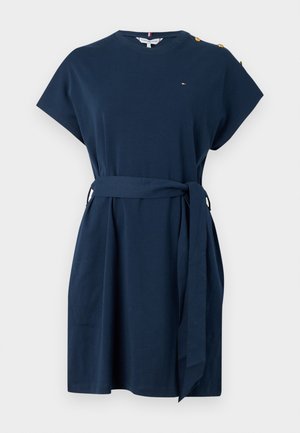 Tumši zilā kokvilnas kleita ar apaļu dekoltē, īsām piedurknēm, sasietu vidukļa jostu un zelta pogu akcentiem uz pleciem.