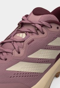 Gros plan d'une chaussure de sport mauve avec des rayures beige pâle, une tige en mesh texturé et des lacets mauves noués sur une languette rembourrée.