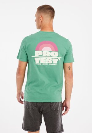 Grøn bomulds T-shirt med et grafisk design med en regnbue og teksten "PRO TEST" trykt på ryggen i hvid og pink.