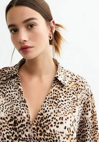 Camicia con stampa leopardata realizzata in un tessuto morbido, con chiusura a bottoni sul davanti, colletto e vestibilità comoda. Presenta macchie nere e marroni su uno sfondo crema.