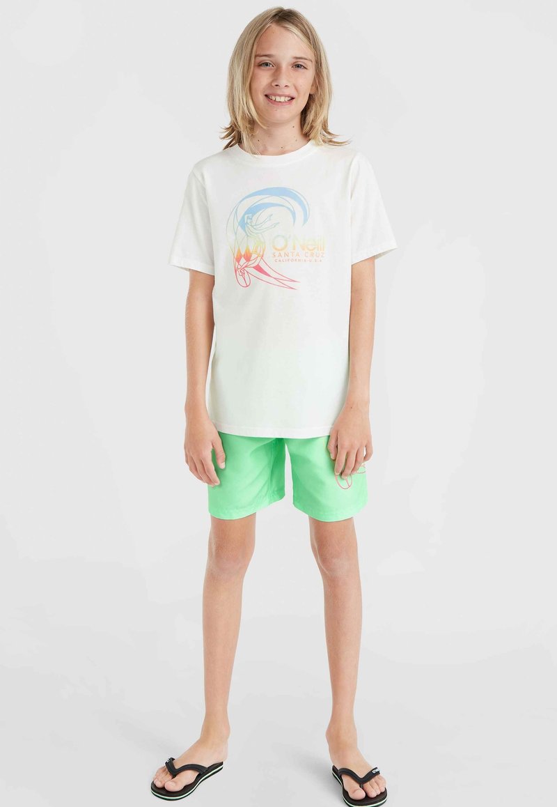 Vit t-shirt med flerfärgad grafik, i kombination med ljusgröna shorts. Bärs tillsammans med svarta flip-flops; avslappnad och ledig passform.